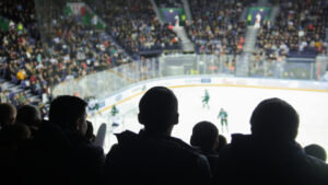 A group of silhouettes of young people watching hockey match in a closed stadium.